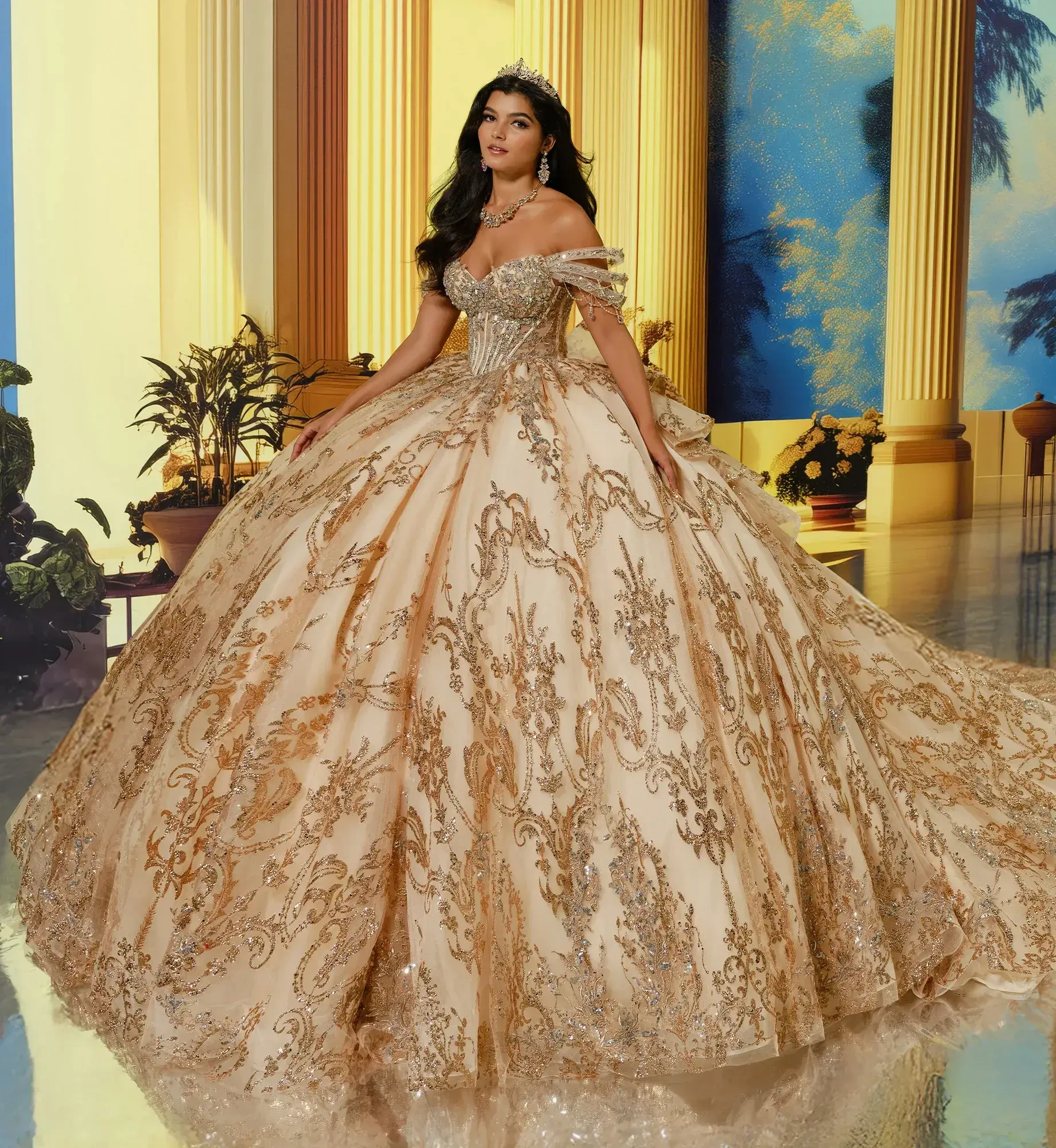 A woman in an elaborate gold and cream gown with off-the-shoulder sleeves, adorned with intricate patterns and embellishments. She has dark, flowing hair and is wearing a tiara. The background features lit columns and tropical plants, creating an elegant setting.