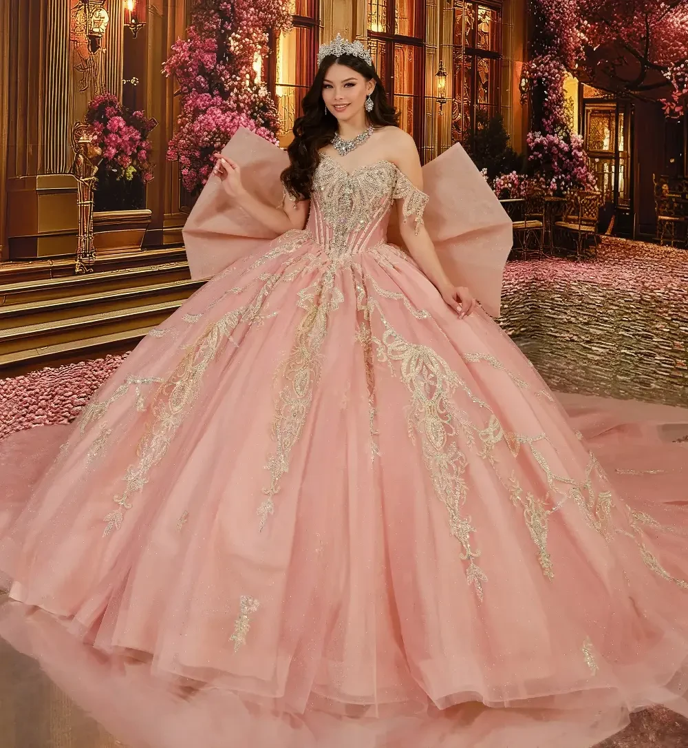 A woman wearing a pink ball gown adorned with gold embroidery, standing in an elegant setting decorated with pink flowers and lavish furnishings.